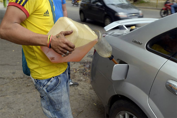 Un hombre vierte gasolina del mercado negro en el coche de un cliente en la calle en Cúcuta, Colombia, el martes 24 de febrero de 2015. 