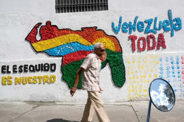 Un hombre camina delante de un mural del mapa venezolano con el territorio del Esequibo incluido, en Caracas, Venezuela [Archivo: Matias Delacroix/AP Photo].