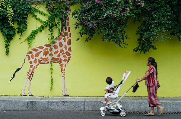 A woman pushes a child in a stroller past a mural of a giraffe in Chengdu, China, on June 5, 2022.
