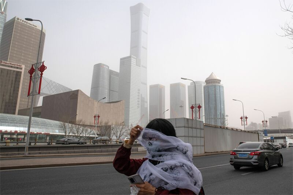 A pedestrian covers her face with a scarf while walking along a road shrouded in smog in Beijing.  