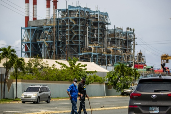 Pedestrians cross a street in front of the Puerto Rico Electric Authority (Prepa) Palo Seco Power Plant in Toa Baja, Puerto Rico, on Friday June 4, 2021. Luma Energy -- a consortium of Atco Ltd. and Quanta Services Inc. working with Innovative Emergency Management Inc. -- took over the operation and management of the Puerto Rico Electric Power Authority's transmission and distribution lines on June 1. , Bloomberg